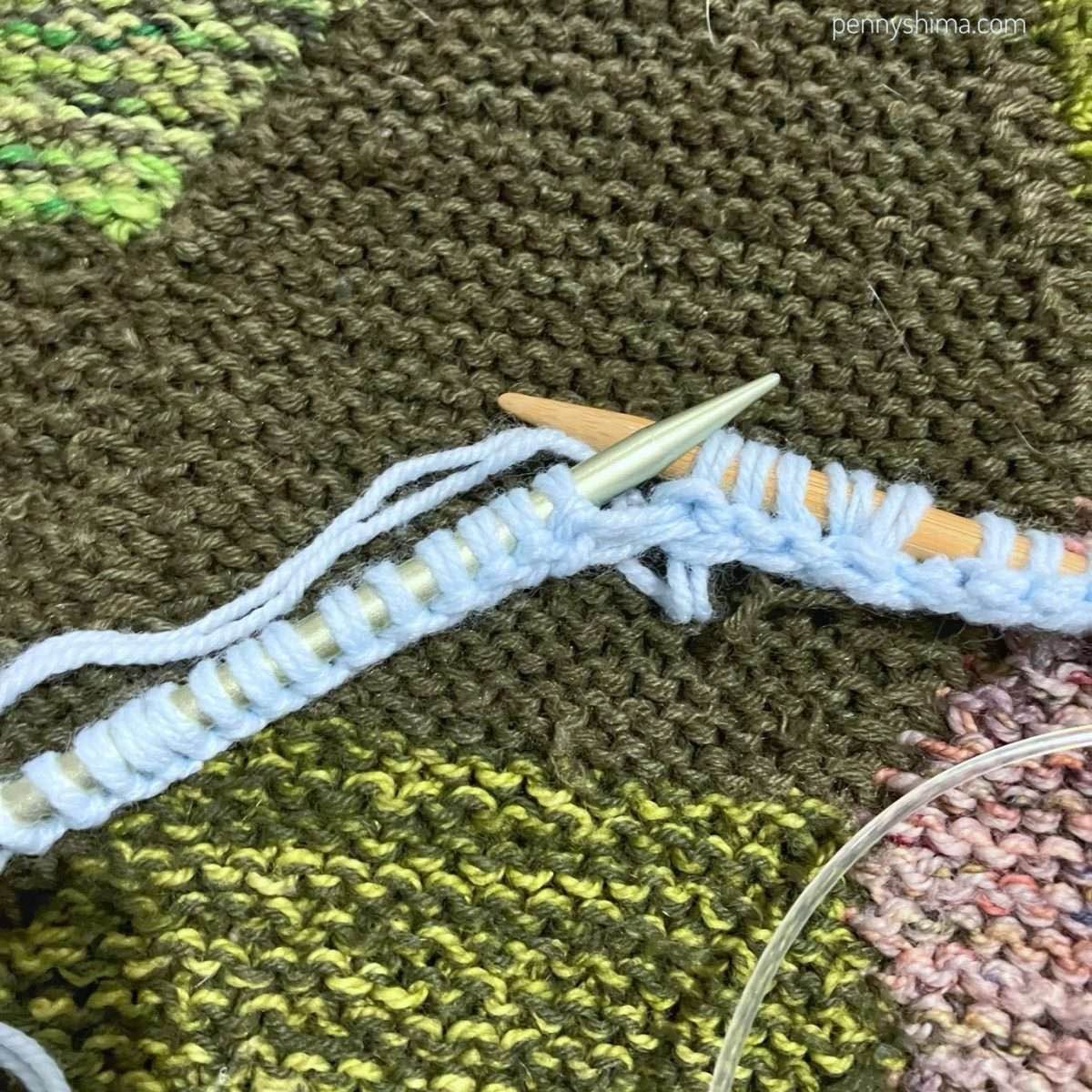 Light blue yarn being knitted off a metal needle onto a bamboo one