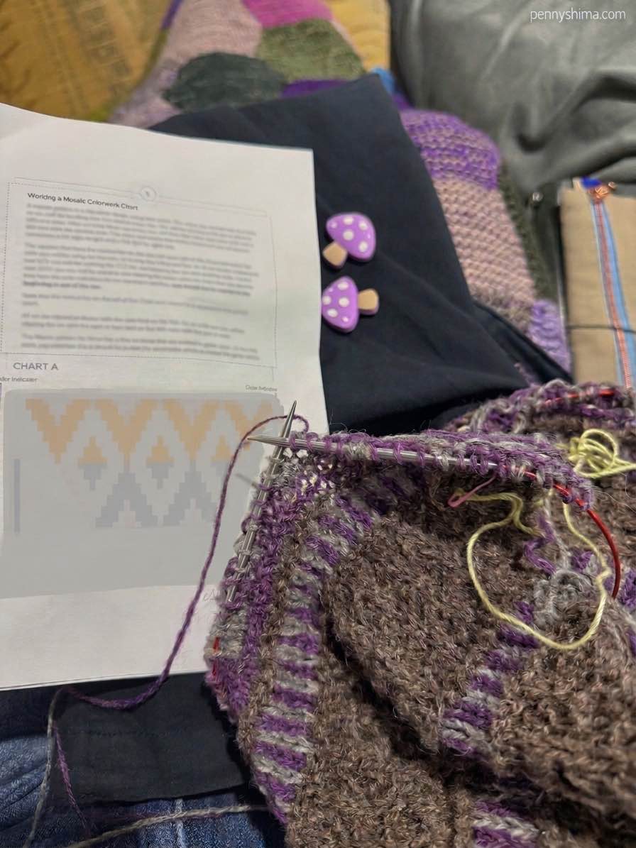 brown knit shawl with purple and light grey mosaic knitting in progress on knitter's lap with shet of instructions visibile