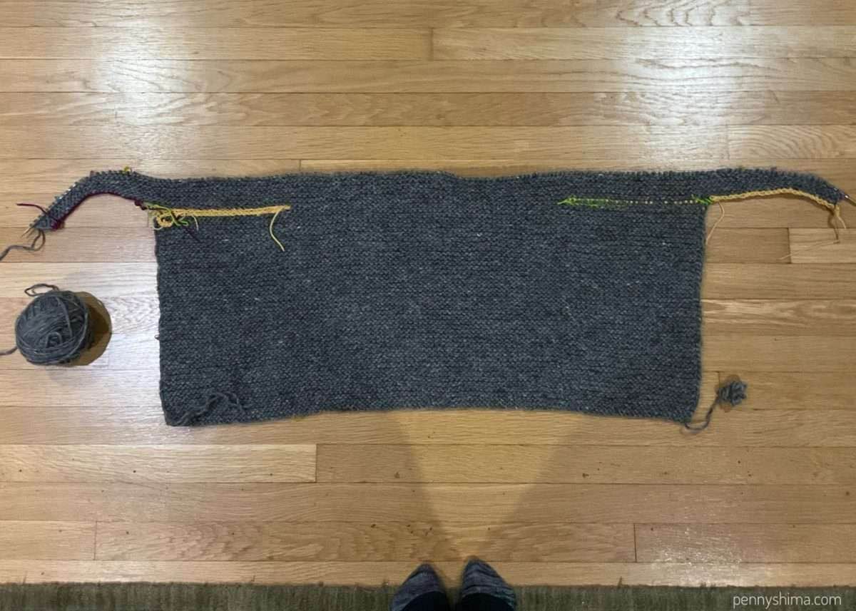 grey bog jacket in progress laid flat on a wooden floor with the sleeves in progress.