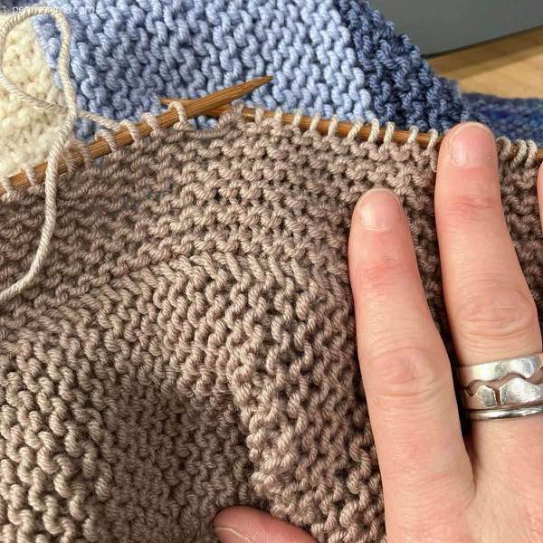 tan sections of garter stitch being worked with blues and ecru in background
