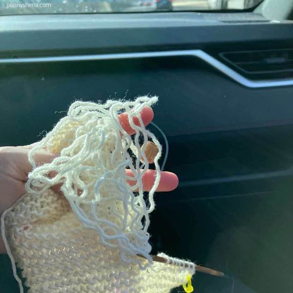 white knit selvedge ripped out being held by a hand in the passenger seat of a car