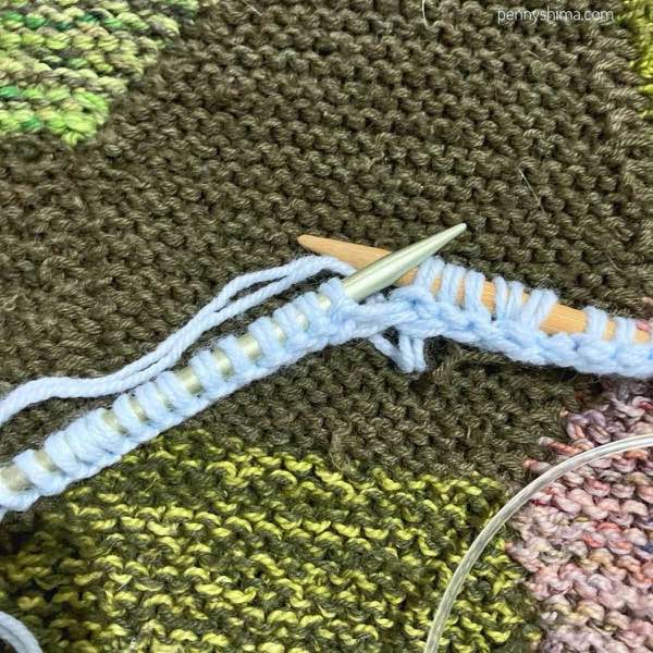 Light blue yarn being knitted off a metal needle onto a bamboo one