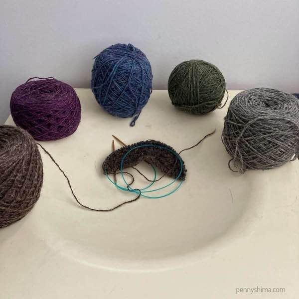 5 balls of Bartlettyarns sport on an off white table. In the center is the start of an Argus Shawl
