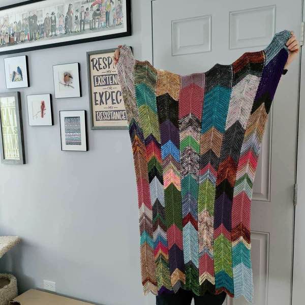 Blanket held up next to a light grey wall and some artwork and posters.