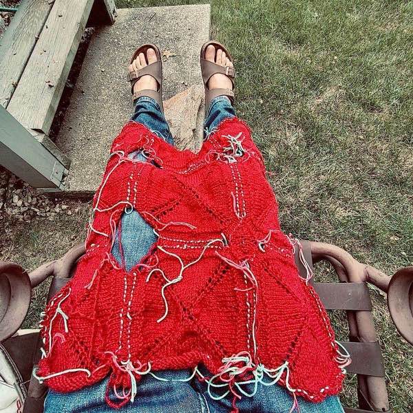 Red blanket shown in progress, 9 squares joined as well as the right internal square. It’s shown laid on a person’s lap. They are wearing jeans with legs extended.