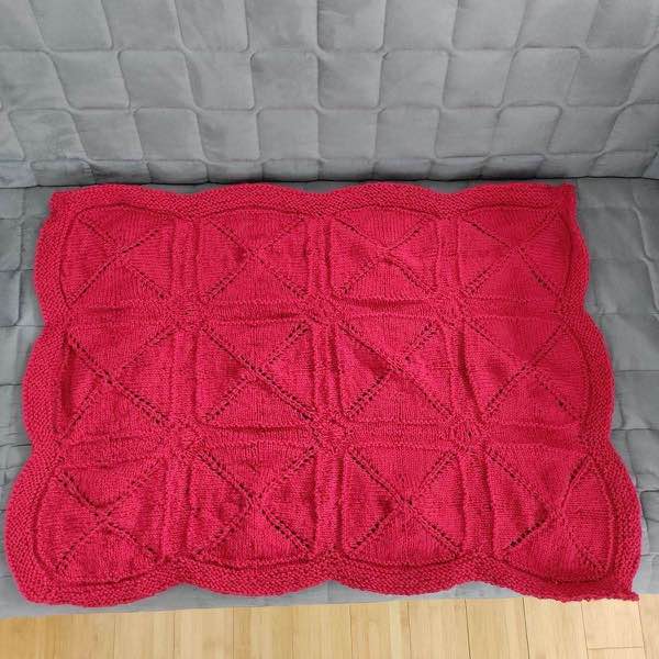 Finished red blanket laying flat on a grey couch.