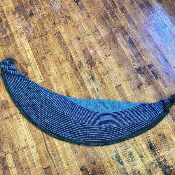 The grey and green striped shawl laid flat on a distressed wooden floor