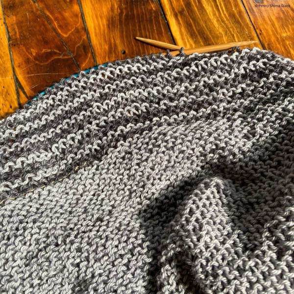 Grey and charcoal striped garter stitch knit shawl in progress shown on a distressed wooden floor