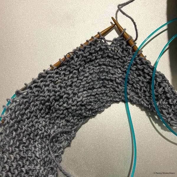 beginning of color affection shawl, a row in progress. yarn is a light grey and it's shown on a silver background