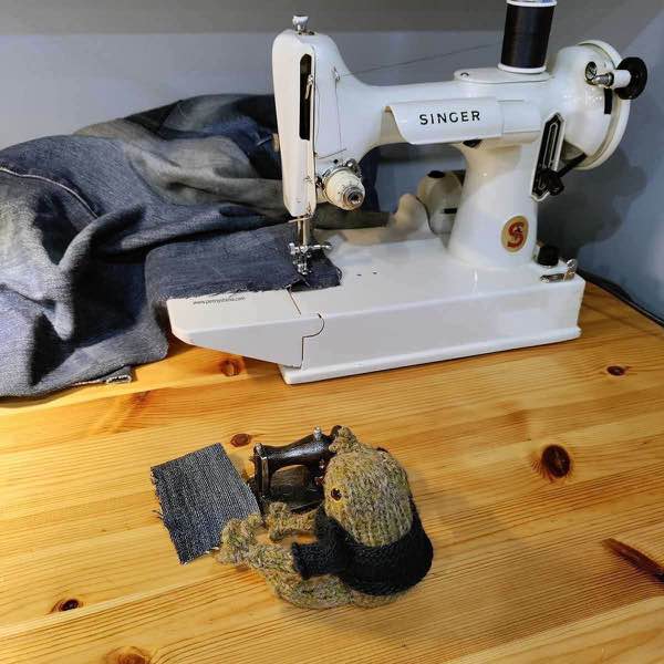 Frog sewing denim at a black sewing machine next to a white singer featherweight