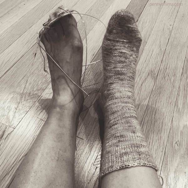 a filtered image with a completed knit sock on the right foot and the very beginning of a toe on the left.