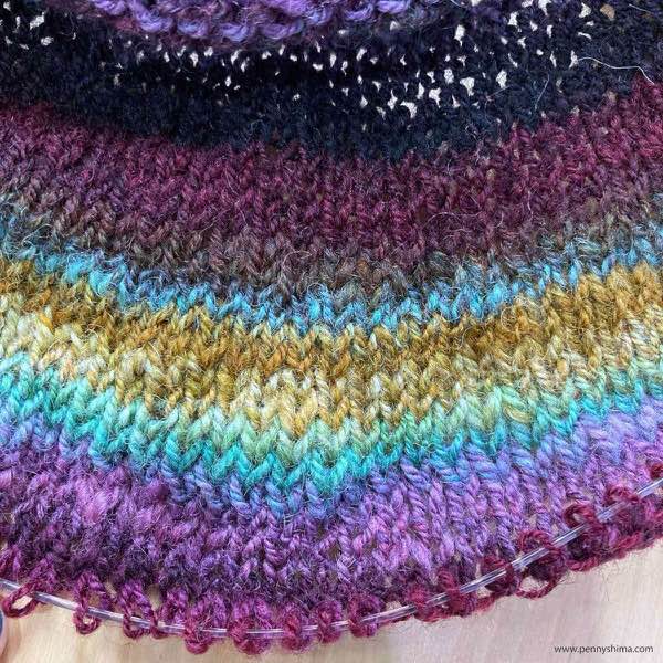Detail of muted rainbow handspun yoke in progress. The colors go from a dark red (nearly black) to deep merlot red, brown, blue, golds, more blues, and now to pink-purple and back to the merlot.