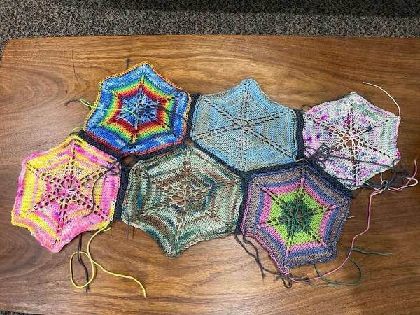 Knit hexagon blanket, six motifs joined, 3 wide and two rows. Laid flat on a wooden table.