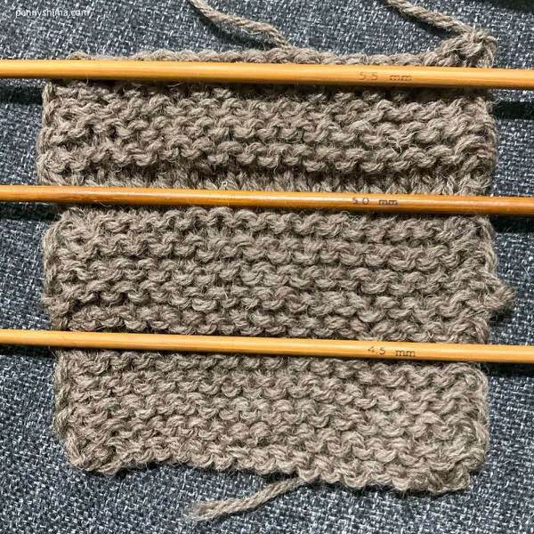 Fishermen's Wool In garter stitch with needles ona grey fabric background