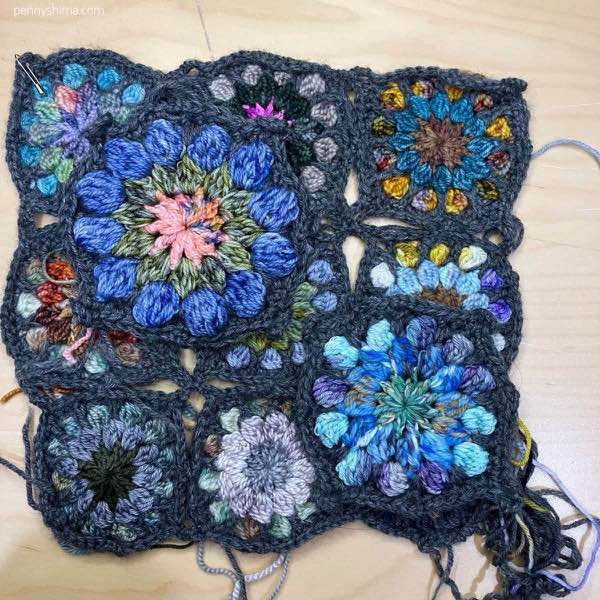 completed crochet motif in dc and hdc shown on a light wooden background on top of a 9-patch of the original sized fingering weight crochet motifs.