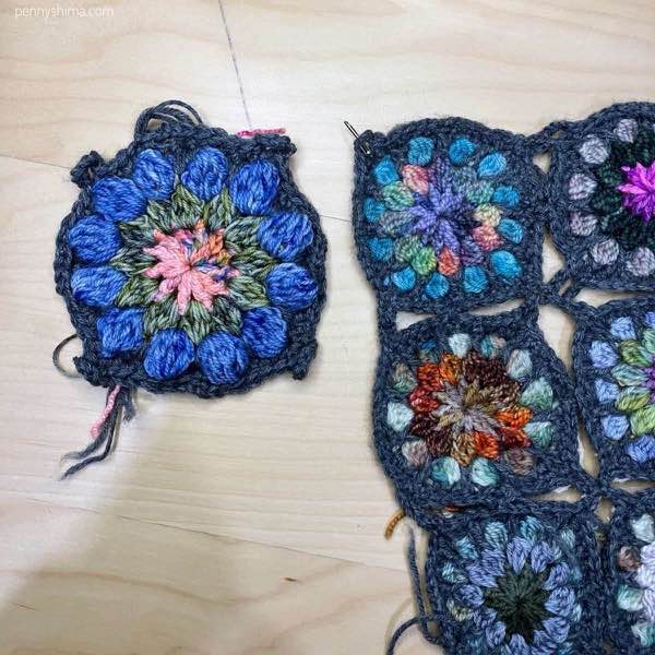 completed crochet motif in dc shown on a light wooden background next to some of a 9-patch of the original sized fingering weight crochet motifs.