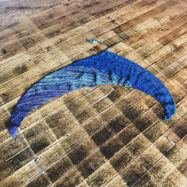 Hand spun and knit shawl laid flat on a wooden floor. The ends are not woven in.