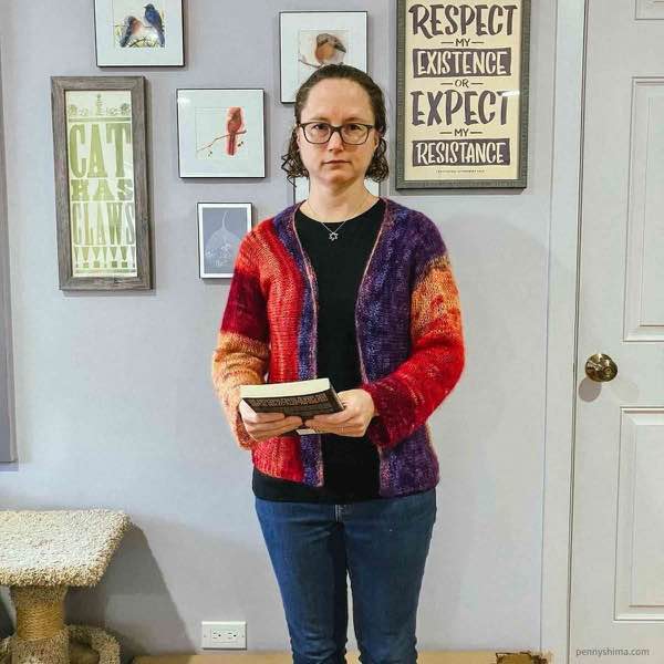 knitter wearing the sandstone striations cardi in front of a light grey wall with artwork.