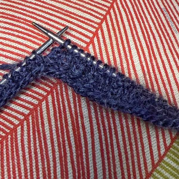 needles showing 1x1 rib of Rhapsody Light in a dark navy on a red "striped" pillow (it's cropped, they're actually leaf shapes)