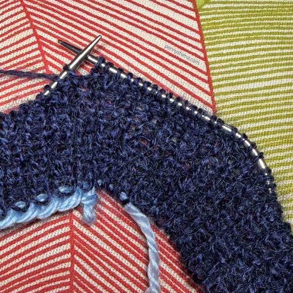 needles showing 1x1 rib of Rhapsody Light in a dark navy on a red & green "striped" pillow (it's cropped, they're actually leaf shapes)