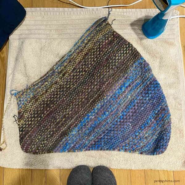 Unblocked shift cowl laid mostly flat on a pale tan towel. A handheld steamer is visible.