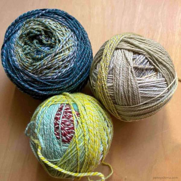 3 balls of Spincycle Yarns dyed in the wool on a light wooden desk.