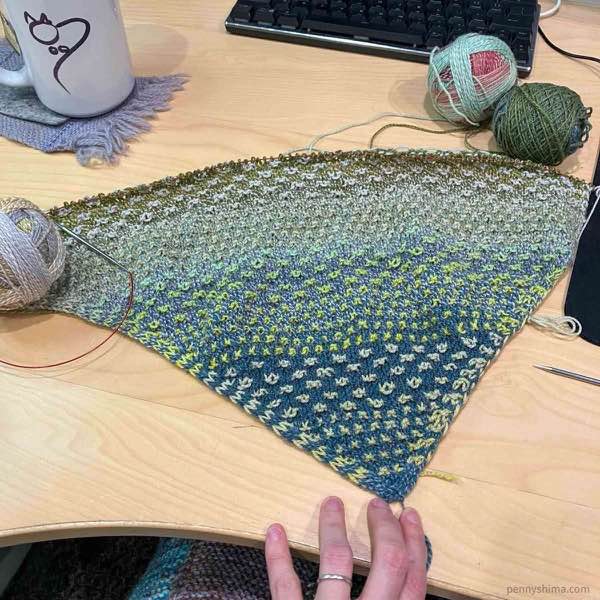 shift cowl, in section 3 in progress laying flat on a light wooden desk.