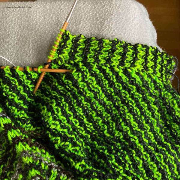 showing knitted on border for front of KAL top. The colors are neon green and a dark brown/black. It is shown on a light grey fleece blanket.