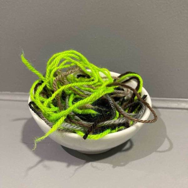 Lots of ends in a small white bowl on a grey shelf against a grey wall.