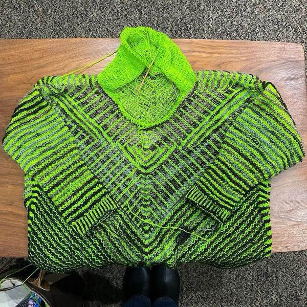 KAL sweater with hood in progress, laid flat on a wooden coffee