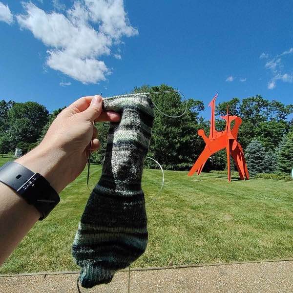 knit sock in progress. shown held up next to "Hats Off" by Alexander Calder at the The Donald M. Kendall Sculpture Gardens at PepsiCo World Headquartersin Purchase, NY