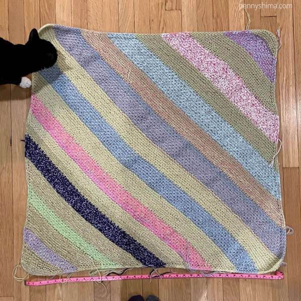 Finished blanket unblocked on a wooden floor with a feline inspector