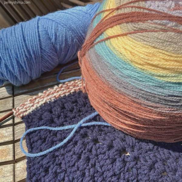 Navy granny square with various yarns on top as the knitter decides colours.