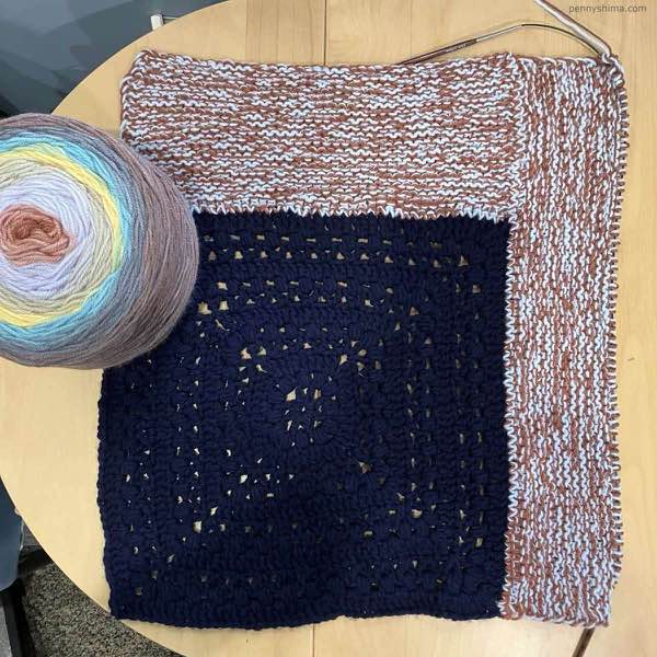 blanket with navy granny square center and garter stitch log cabin stripes in progress.