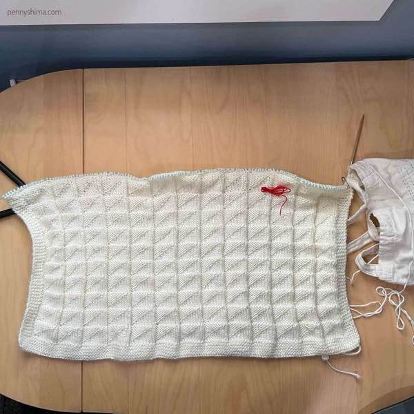 a white knit blanket in progress on a wooden desk.