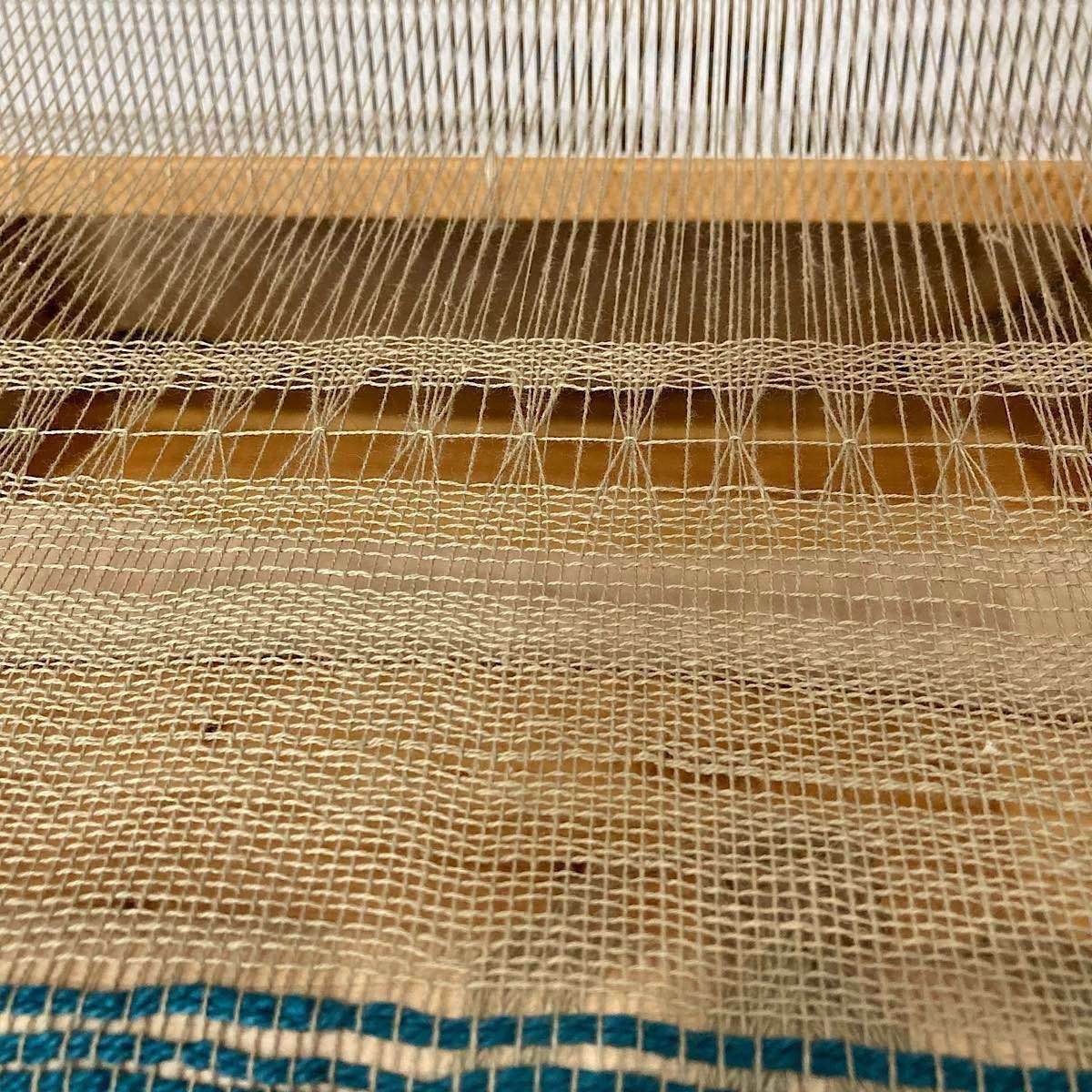 beginning of 20/2 warp & weft weaving on a rigid heddle loom. some of the teal 3/2 cotton, held doubled is visible in the bottom. Then some rows of semi-evenly woven tabby, followed by the first brooks bouquet followed by more even pics.